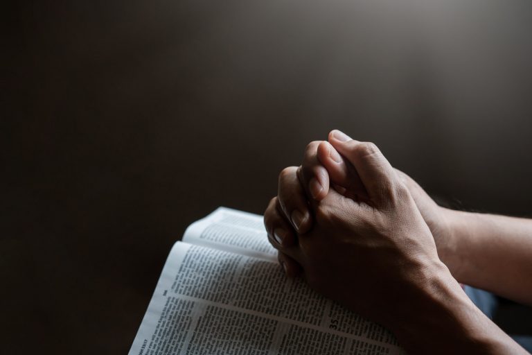 Hands together in prayer to God along with the bible In the Christian concept of faith