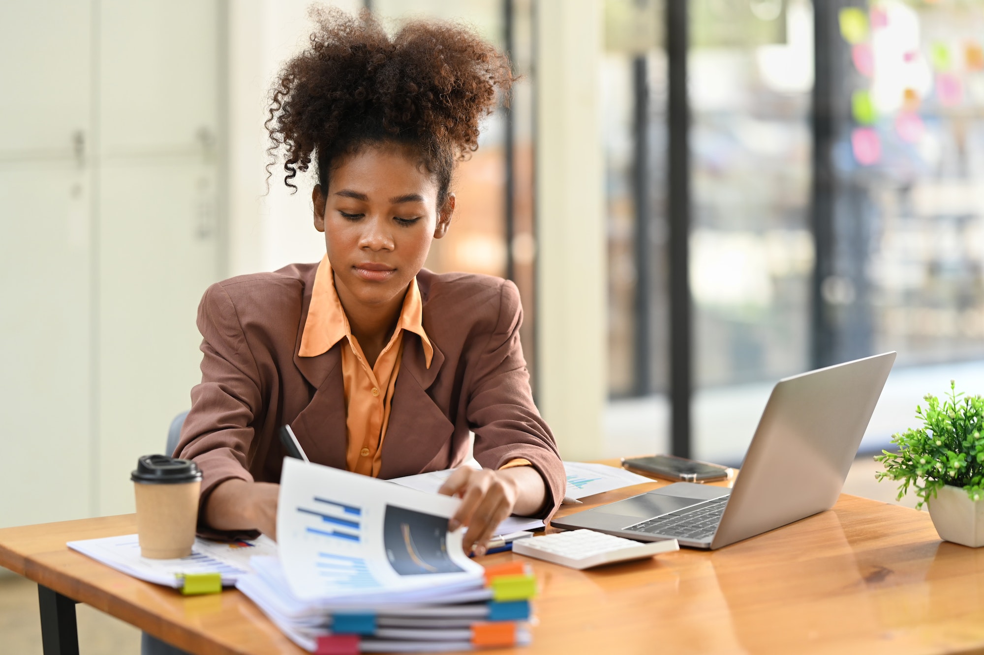 Concentrated African American female economist analyzing financial data and using laptop.